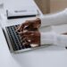 Close-up of woman's hands typing on a laptop in a modern home office setting.