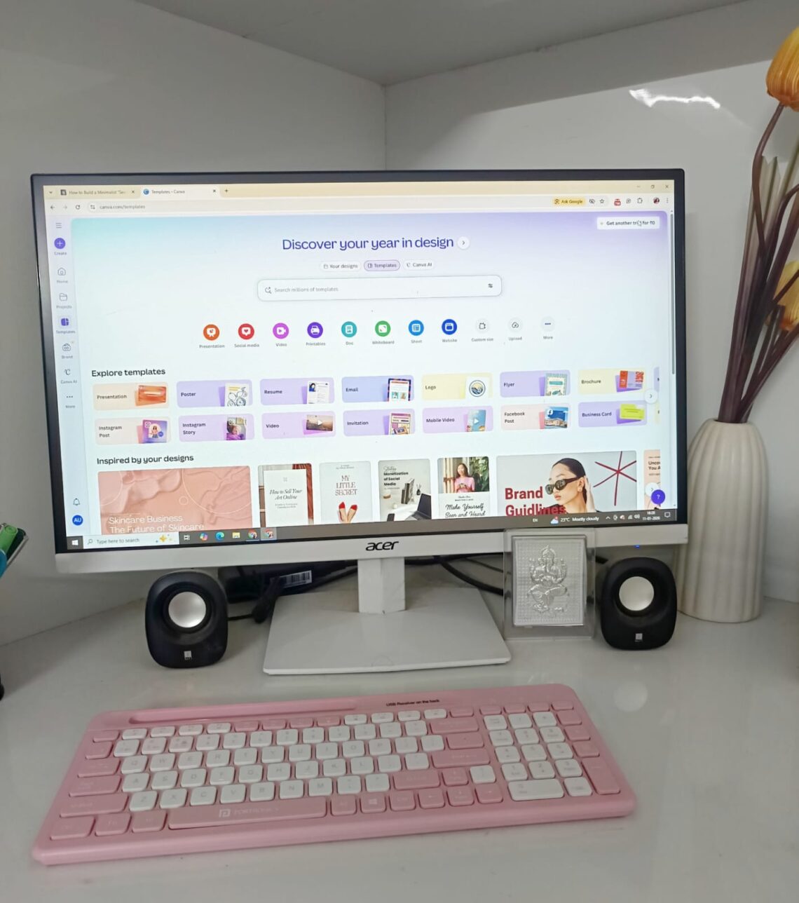 A minimalist workspace with a pink keyboard and a monitor showing the Canva template dashboard.