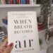 When Breath Becomes Air – Book Review Hand holding the book When Breath Becomes Air by Paul Kalanithi in front of a bookshelf.